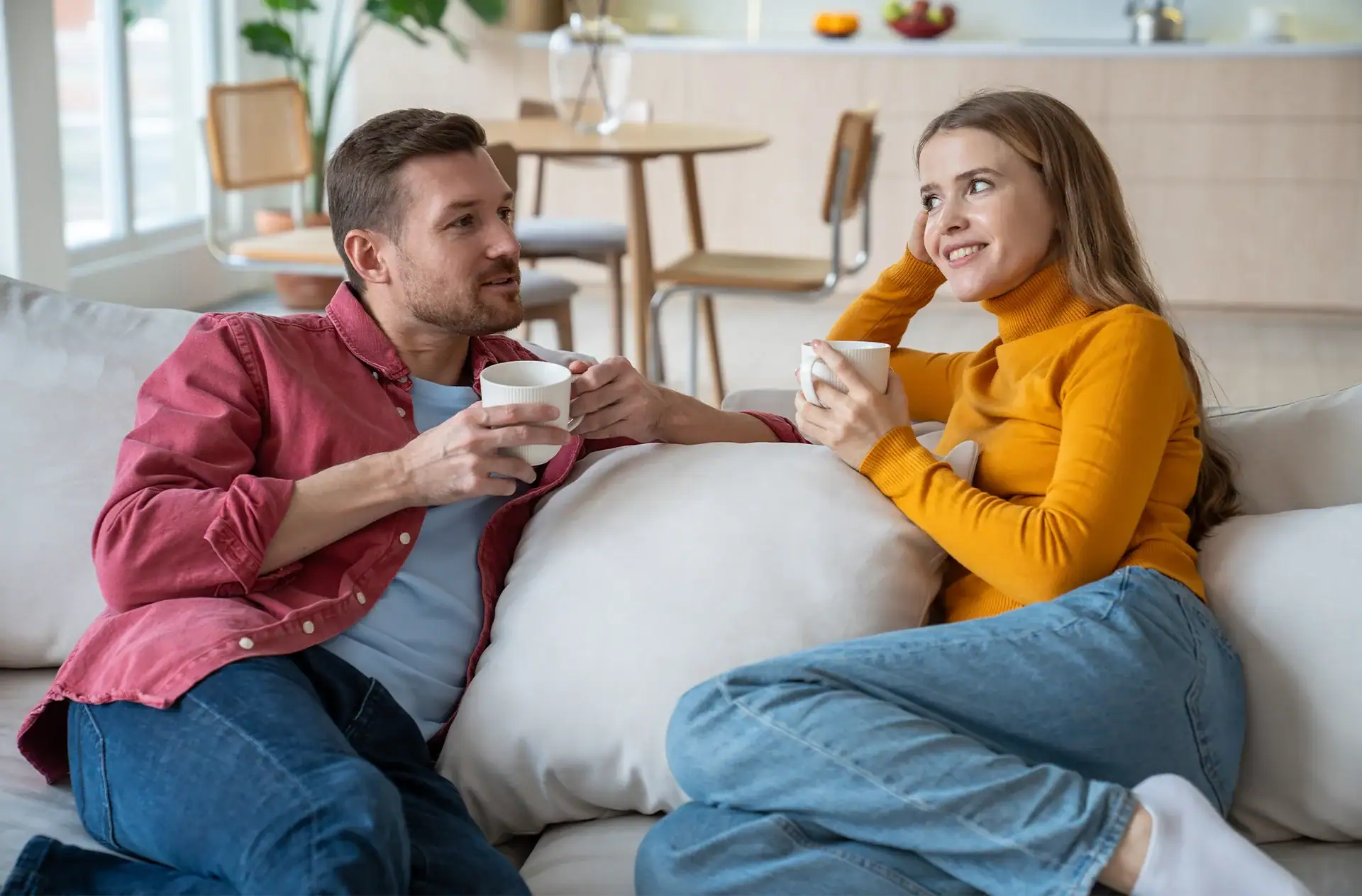 pleased couple man woman talking sitting on home couch drinking coffee enjoying communication