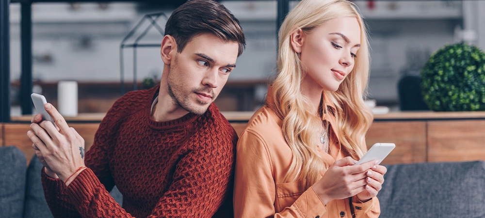 young couple sitting back to back and using smartphones, jealousy concept