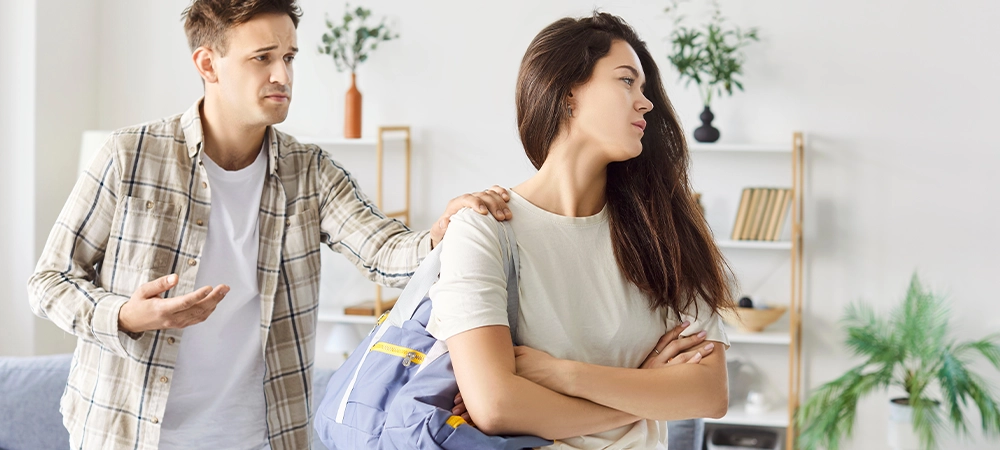 Young couple breaking up and ending relationship after argument. Wife with packed bag leaves her frustrated husband and go away. Guilty man tries to stop girl but she doesn't want to listen to him.