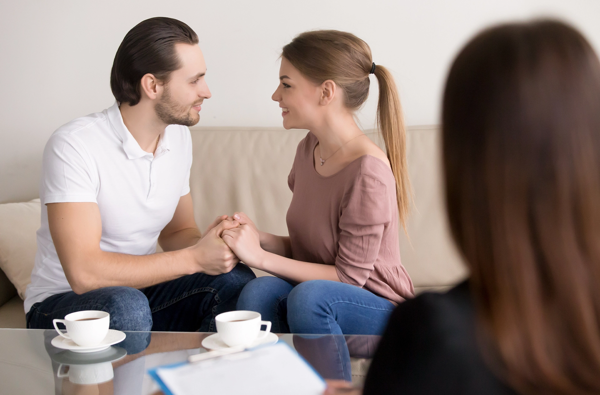 Excited loving couple sitting on sofa holding hands looking in the eyes, meeting with wedding planner, choosing place for honeymoon trip, successful marriage therapy with family psychologist